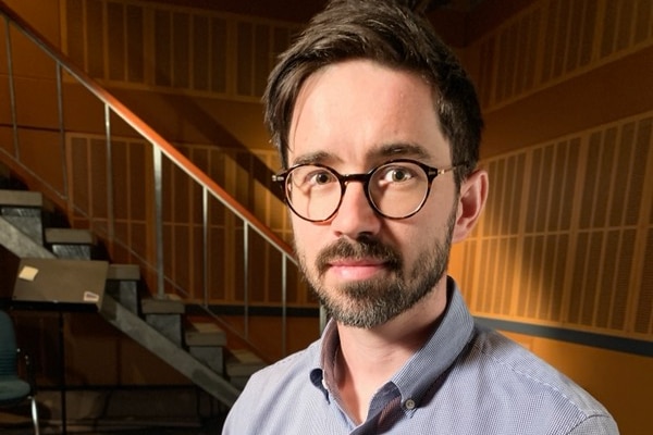 A young man with glasses and a short beard looking at the camera