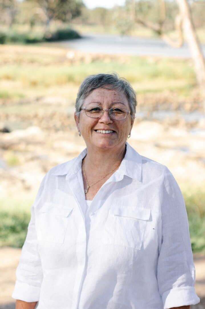 An Aboriginal woman with short hair and a white shirt smiles at the camera/