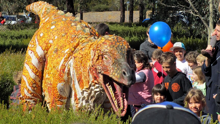 A dinosaur walks through crowds at the Geoscience Australia open day.