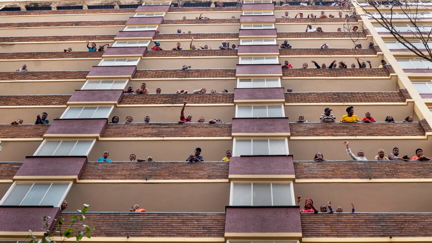 Johannesburg residents confined in an attempt to prevent the spread coronavirus, stand and wave from their balconies