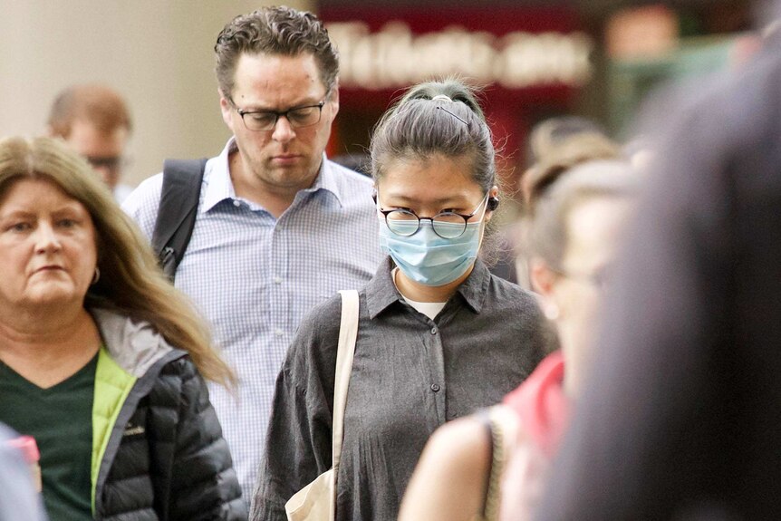 Group of people walking in Melbourne's CBD with one woman wearing a surgical mask.
