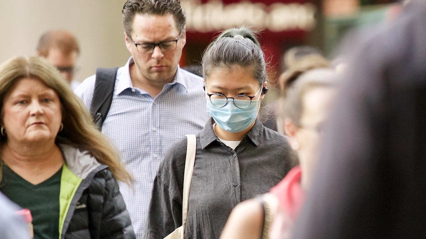 Group of people walking in Melbourne's CBD with one woman wearing a surgical mask.