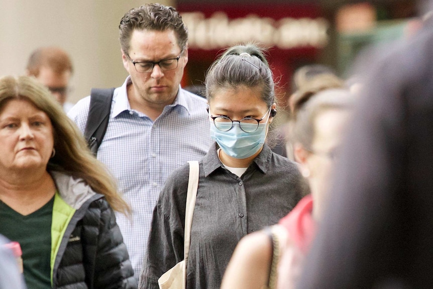 Group of people walking, one wearing a mask.