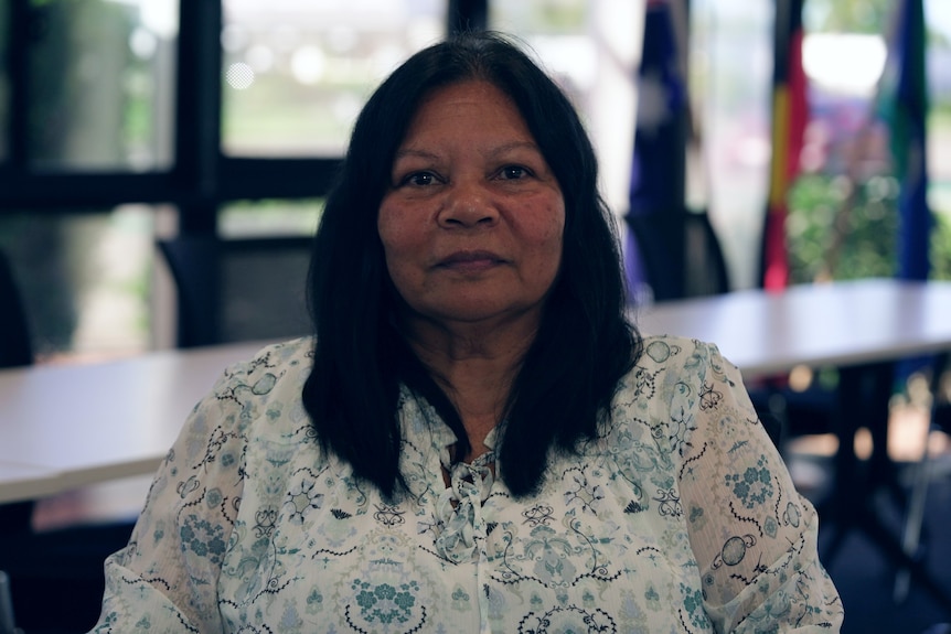 Brenda Lucas in an office with the Australian, Torres Strait and Aboriginal flags in the backgrounds.