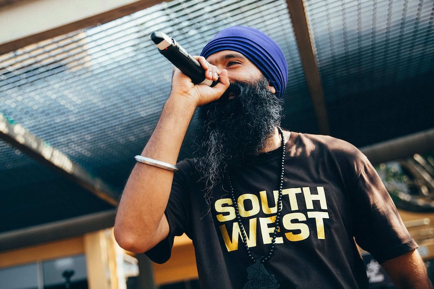 L-FRESH rapping on stage with a microphone in hand, wearing tee-shirt with 'South West' on it.