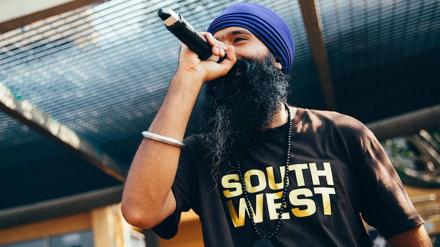 L-FRESH rapping on stage with a microphone in hand, wearing tee-shirt with 'South West' on it.