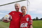 Two girls wearing red tops smiling and holding a soccer ball. 