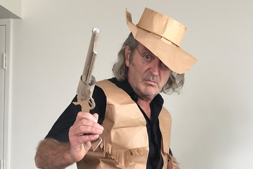 A man wearing a cowboy outfit made out of paper bags posing with a fake pistol.