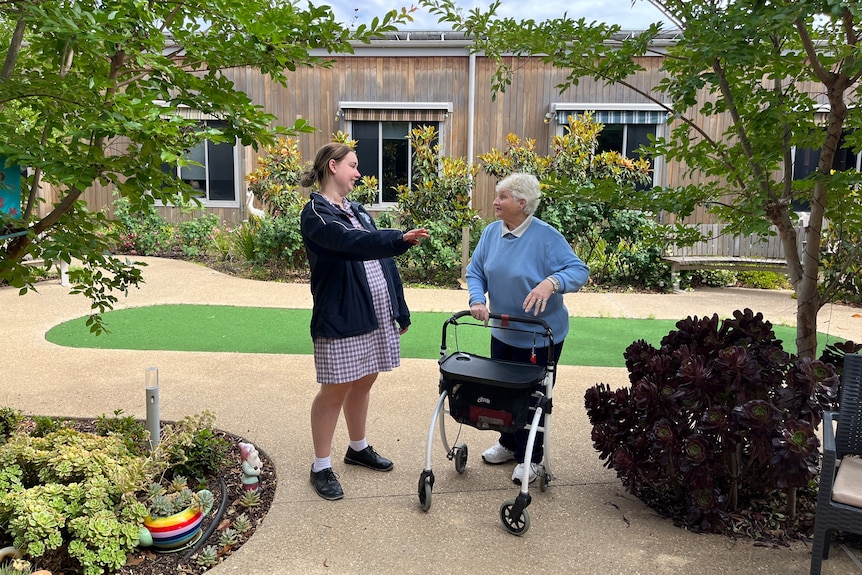 A students speaking to an elderly resident in a garden.