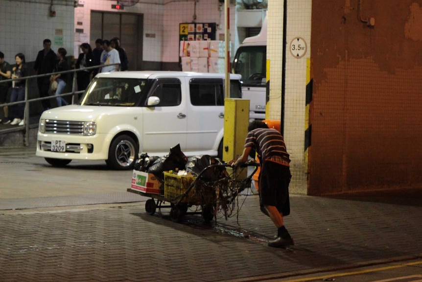 An elderly man pushing a trolley into a recycling plant at night