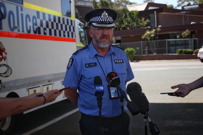 A police officer addresses media while standing in front of a police van