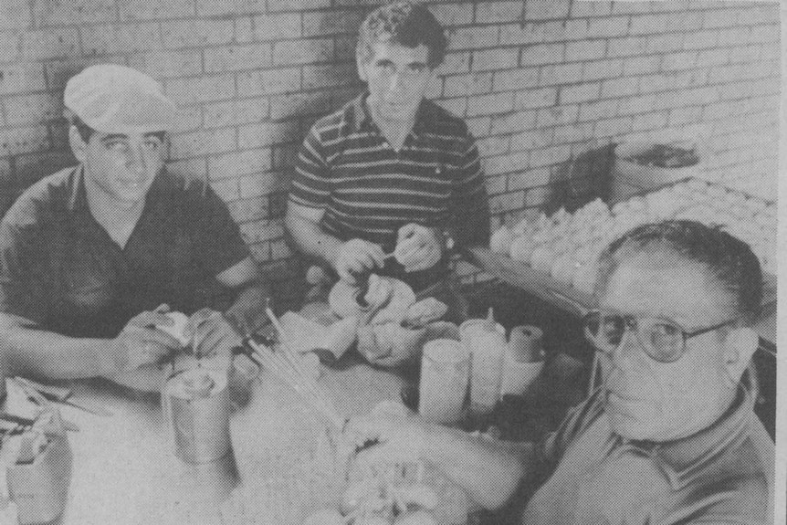 Three men of different ages sit around a table with fireworks in front of them.