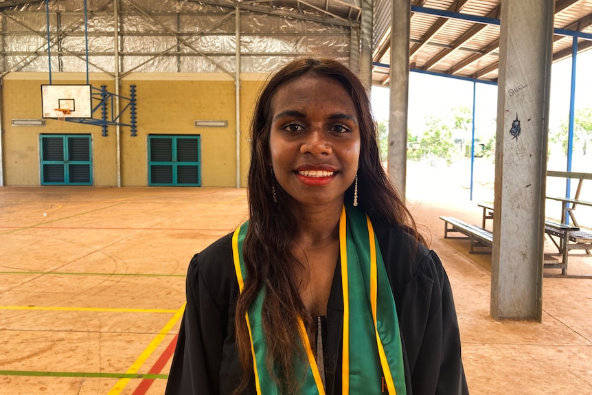 Jazzy Dummo, a student at the college, smiles into the camera. She is standing outside, next to a basketball court.