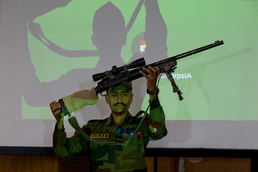 An Indian soldier holds a rifle with a telescopic site over his head.