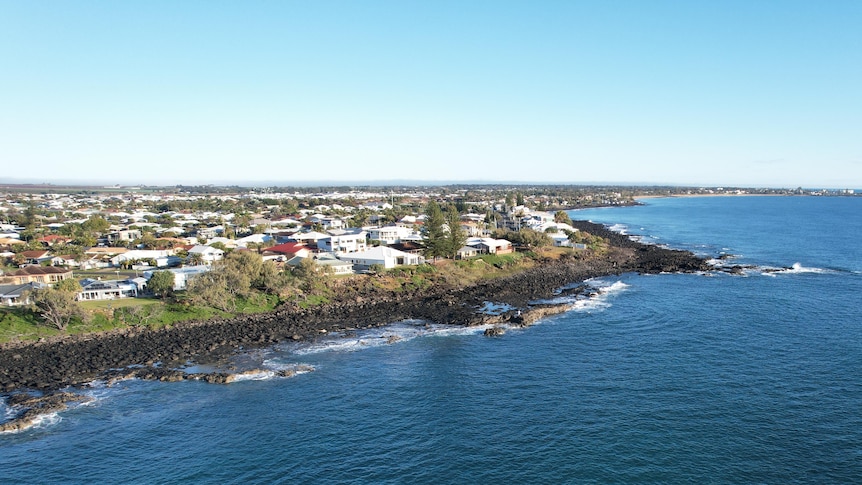 A bird's eye view of a coastline with boats in the water, houses on the land