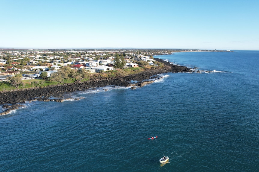 A bird's eye view of a coastline with boats in the water, houses on the land