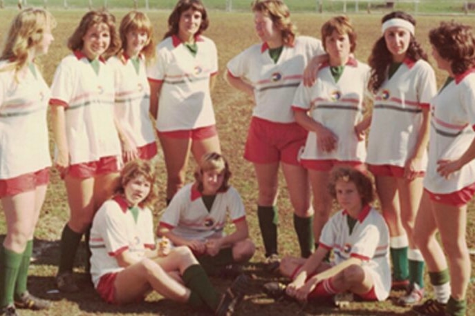 A women's soccer team from the 1970s wearing white shirts with red shorts and green socks