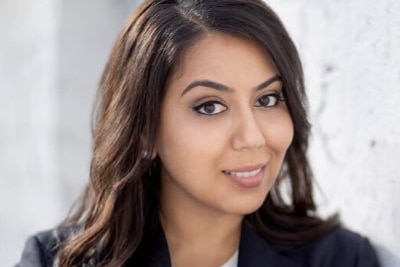 A photo of Mariam Veiszadeh smiling, without hijab, wearing a black blazer.