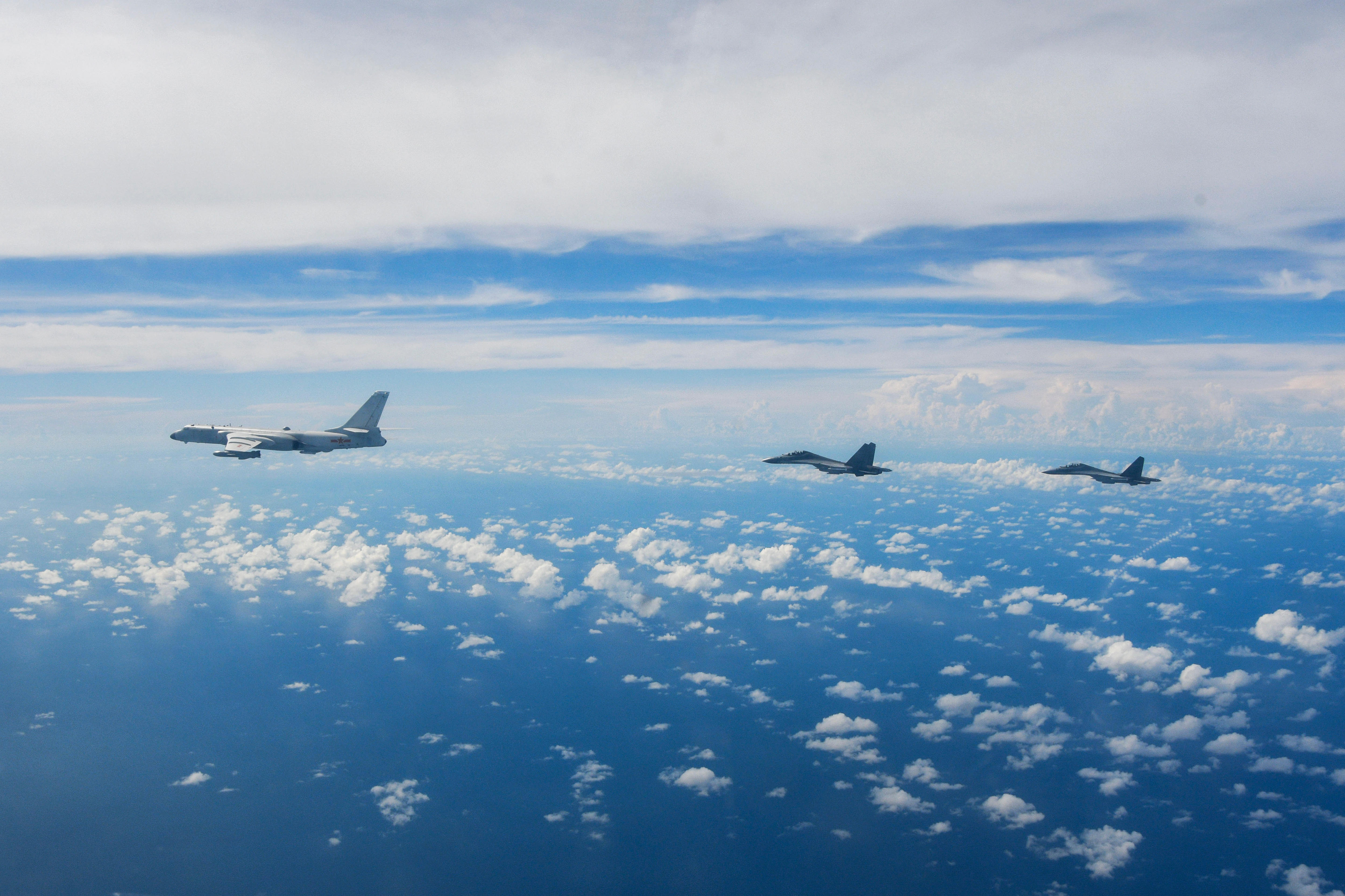 Three military aircraft fly against a bright blue sky dotted with small white fluffy clouds
