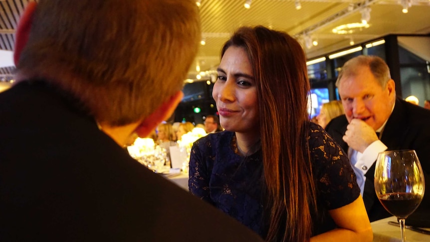 Khara Williams talks to a man with his back to the camera, while Robert Doyle sits behind her, looking into the camera.