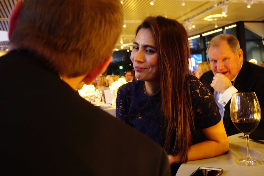 Khara Williams talks to a man with his back to the camera, while Robert Doyle sits behind her, looking into the camera.