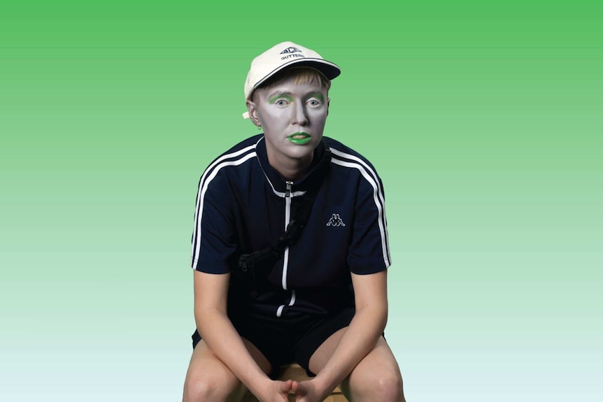 Portrait of artist EO Gill, wearing green lipstick and eyeshadow, against green background.