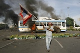 A supporter of ousted Thai PM Thaksin Shinawatra waves the national flag in front of a burning bus