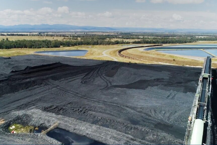 An aerial view of coal extracted from the Narrabri mine, with a landscape of lakes and mountains behind it. 