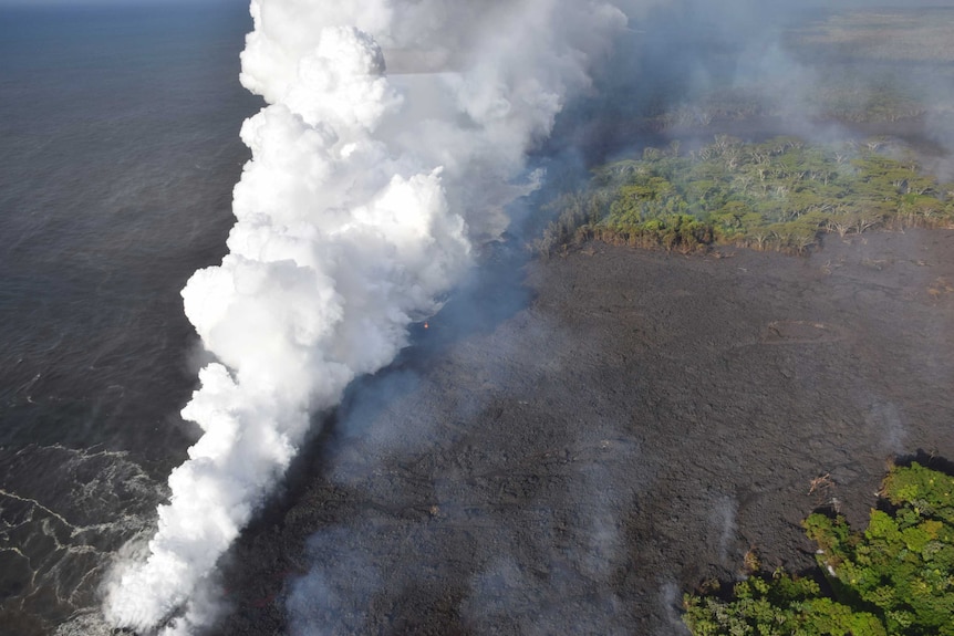 Lava enters the ocean sending and smoke billows into the sky.