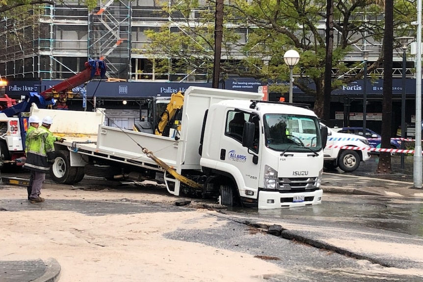 A truck with its front in a hole in the road surrounded by water.