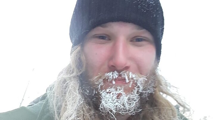 A man wearing a beanie and with snow on his beard.