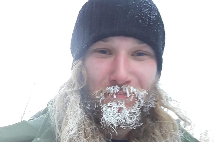 A man wearing a beanie and with snow on his beard.