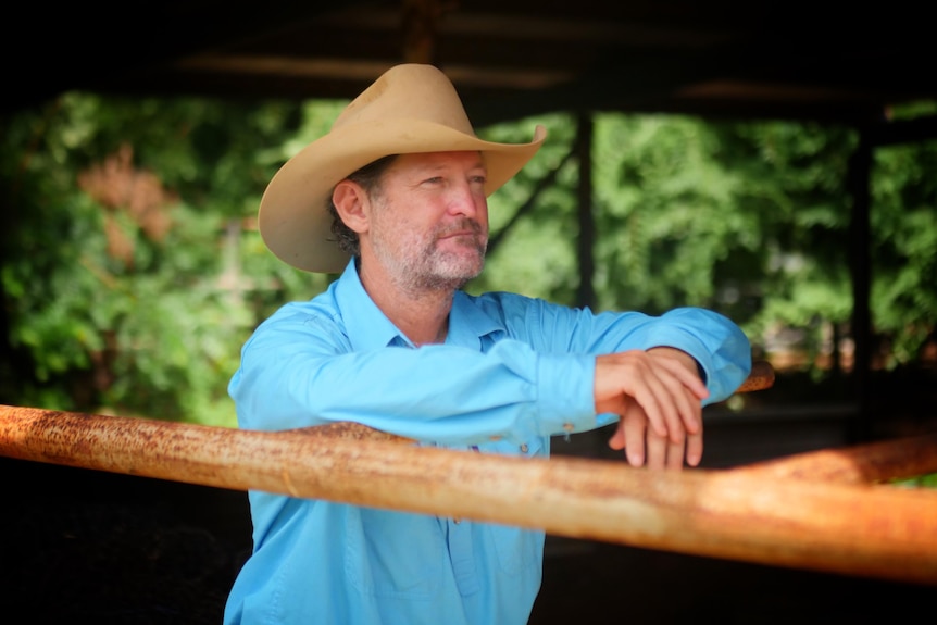 Middle-aged man in Akubra hat  looking out onto farmland. 