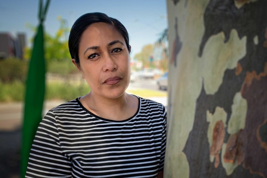 A woman stands next to a tree on a bright blue sky day.