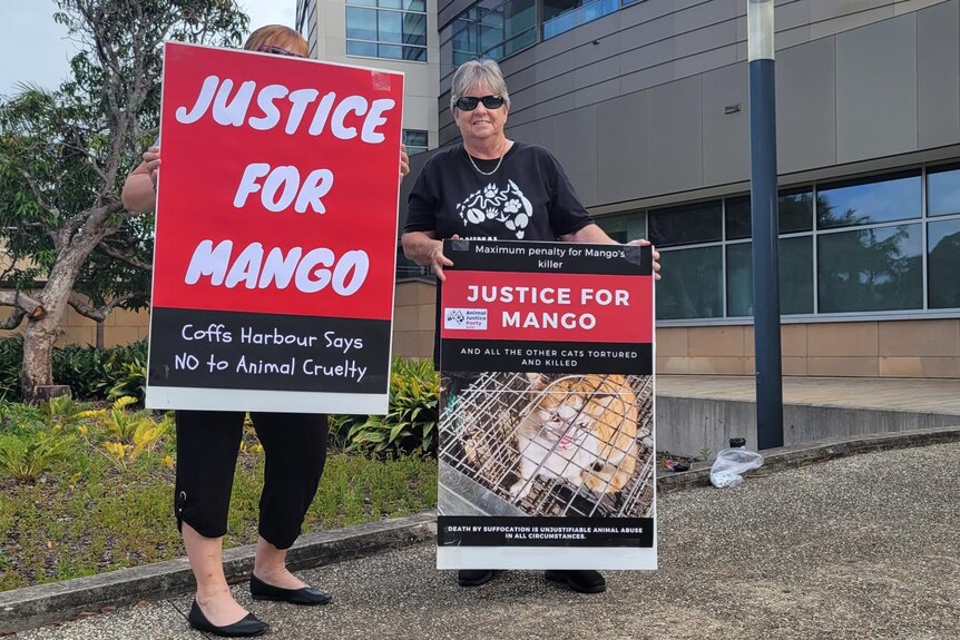 Two women hold large placards, one featuring a picture of a ginger cat, that say "Justice for Mango".
