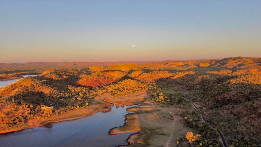 An aerial view of land near Mount Isa, featuring hills and a river bathed in sunlight.