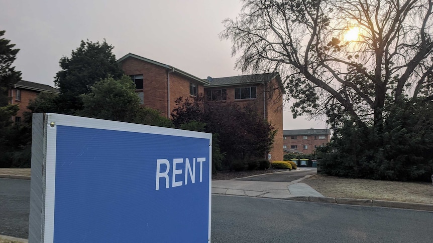 Blue 'rent' sign outside apartment block.