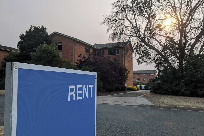 Blue 'rent' sign outside apartment block.