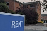 Blue 'rent' sign outside apartment block.