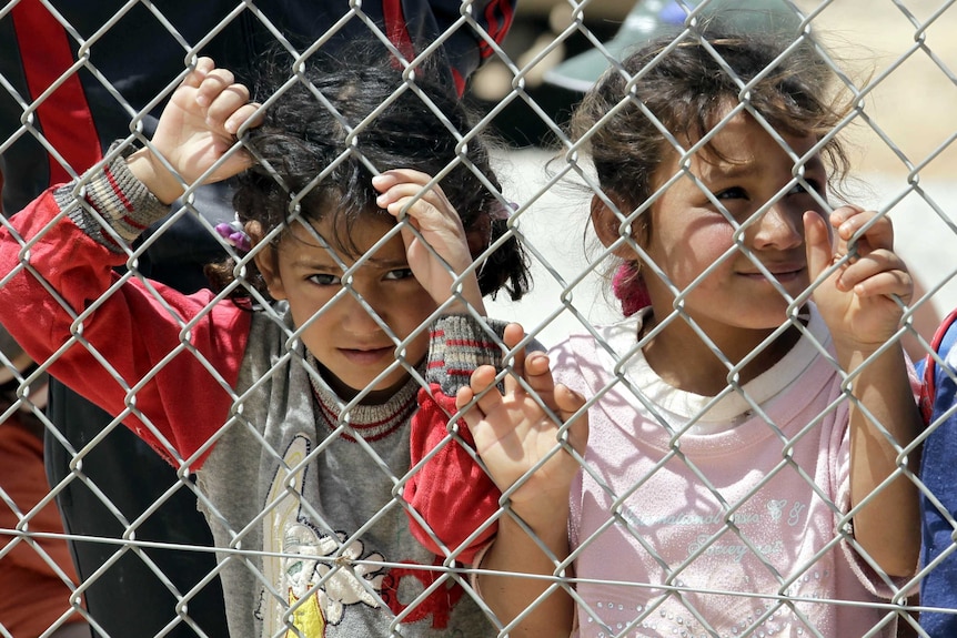 A child in a refugee camp stares through a fence