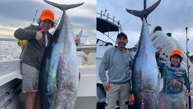 A boy wearing an orange sports cap has a huge grin on his face standing next to a tuna that is longer than him. 