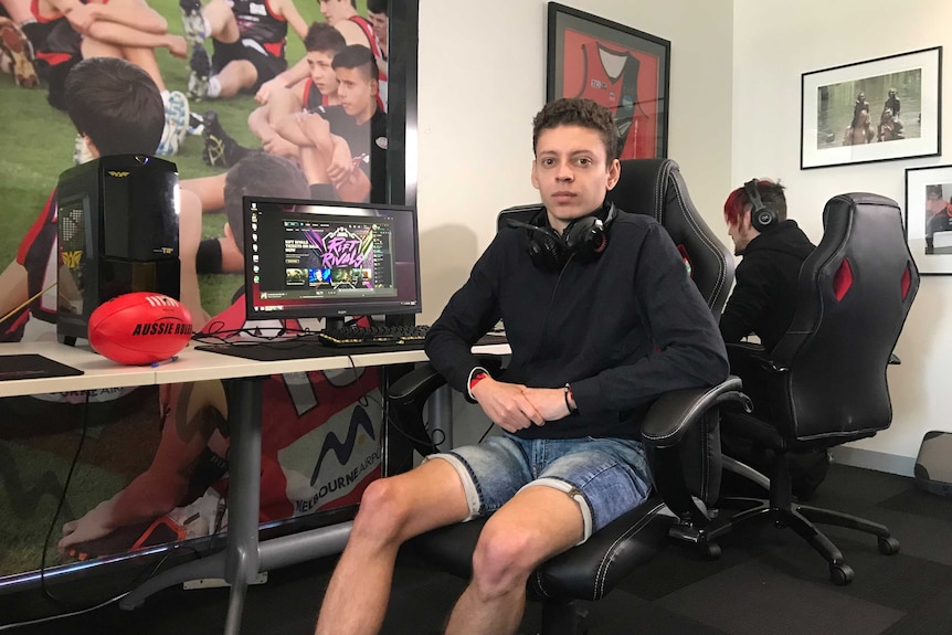 Essendon Esports player Alan Roger sits next to a computer on which he plays League of Legends, in background is his teammate