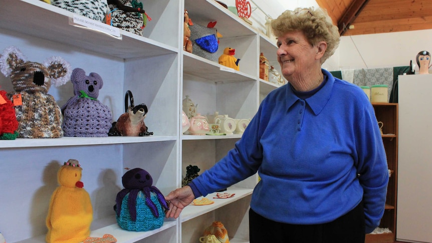 Volunteer and curator Elsie Winter standing next to shelves of tea cosies.