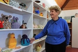 Volunteer and curator Elsie Winter standing next to shelves of tea cosies.