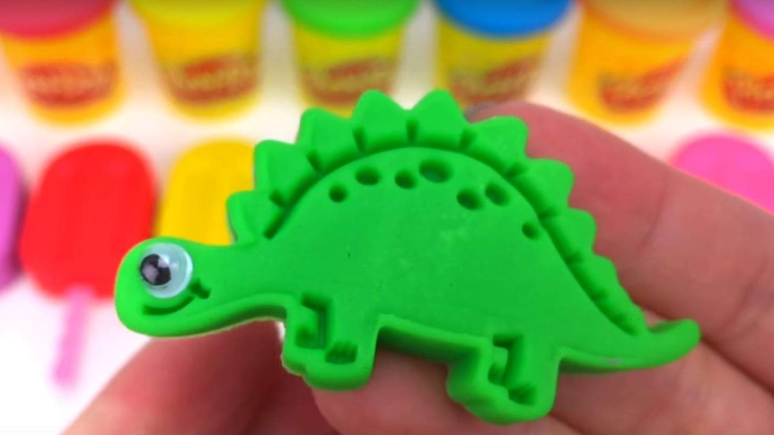 A pair of hands holds a green plasticine dinosaur.