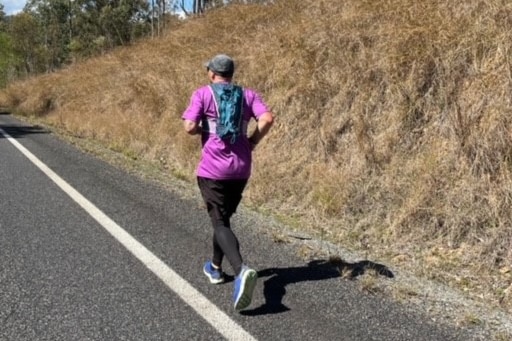 A man in a purple shirt runs along a highway