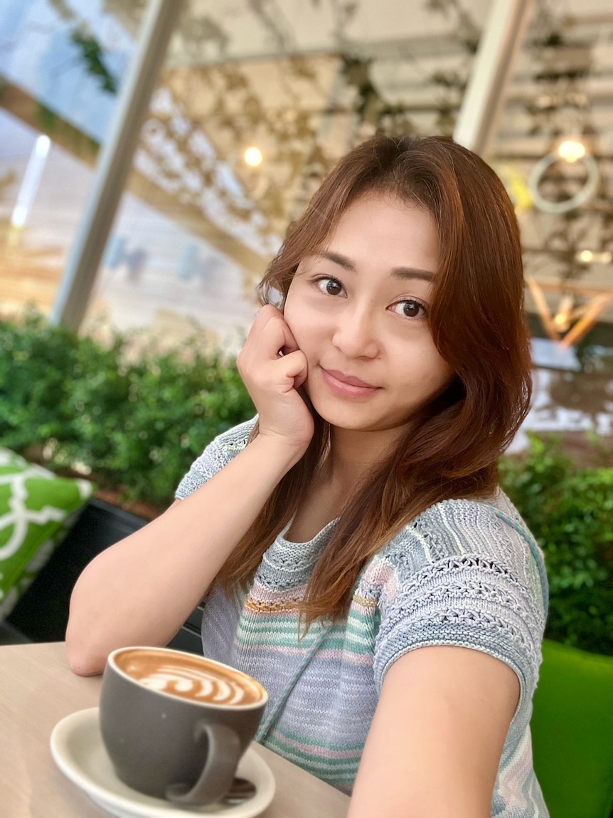 A woman with brown hair taking a selfie at a table with a coffee cup