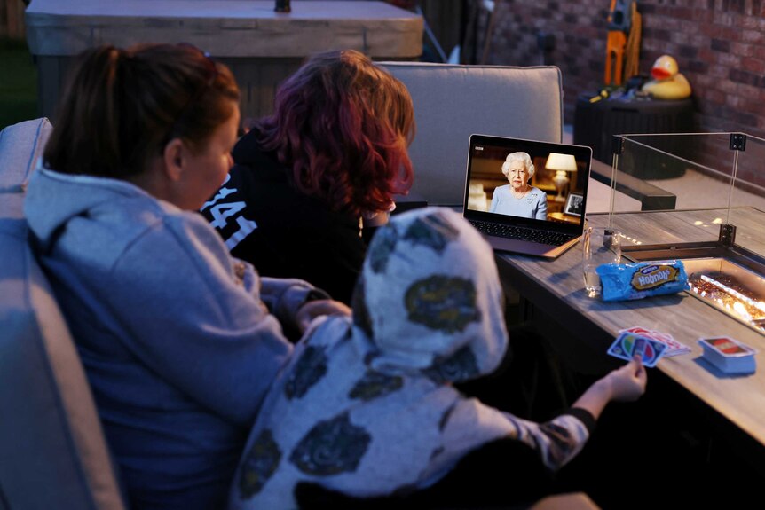 A family huddle around a laptop watching the Queen