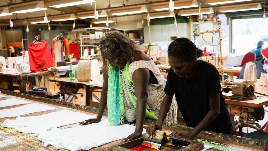 Two women stand at a table in a clothing print shop working on tshirt prints