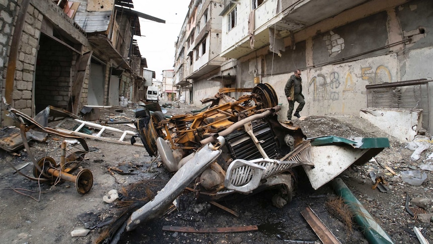 A man walks in the yard of an apartment building damaged by shelling and strown with rubbish.